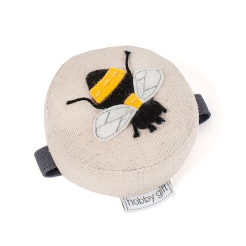 Beige bee pincushion with wrist strap, round fabric pouch with stitched bee appliqué.