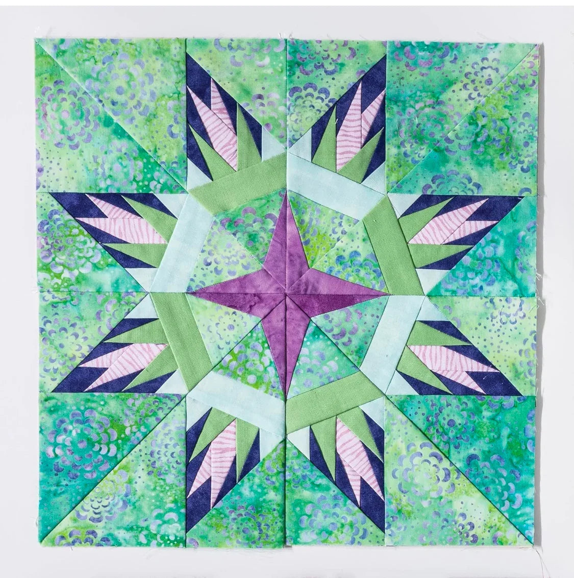 Paper-pieced star quilt block with aqua and green fabric, purple center, and navy accents