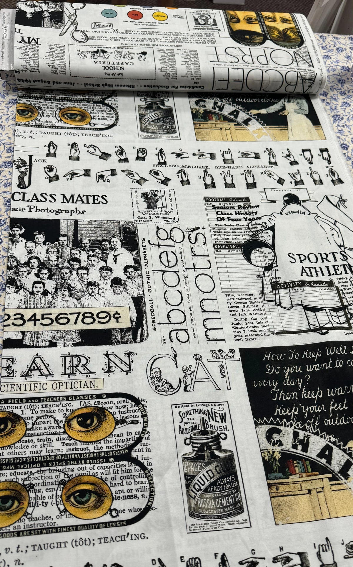 White printed fabric with collage of school graphics, numbers, letters, and classroom icons.