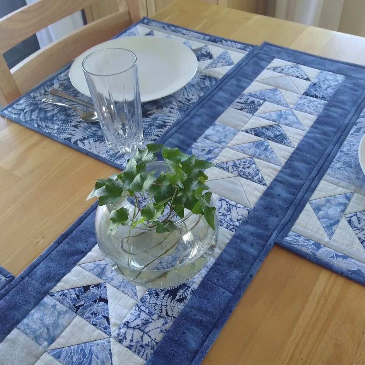 Blue flying geese quilt runner on a wooden table with plates and glass