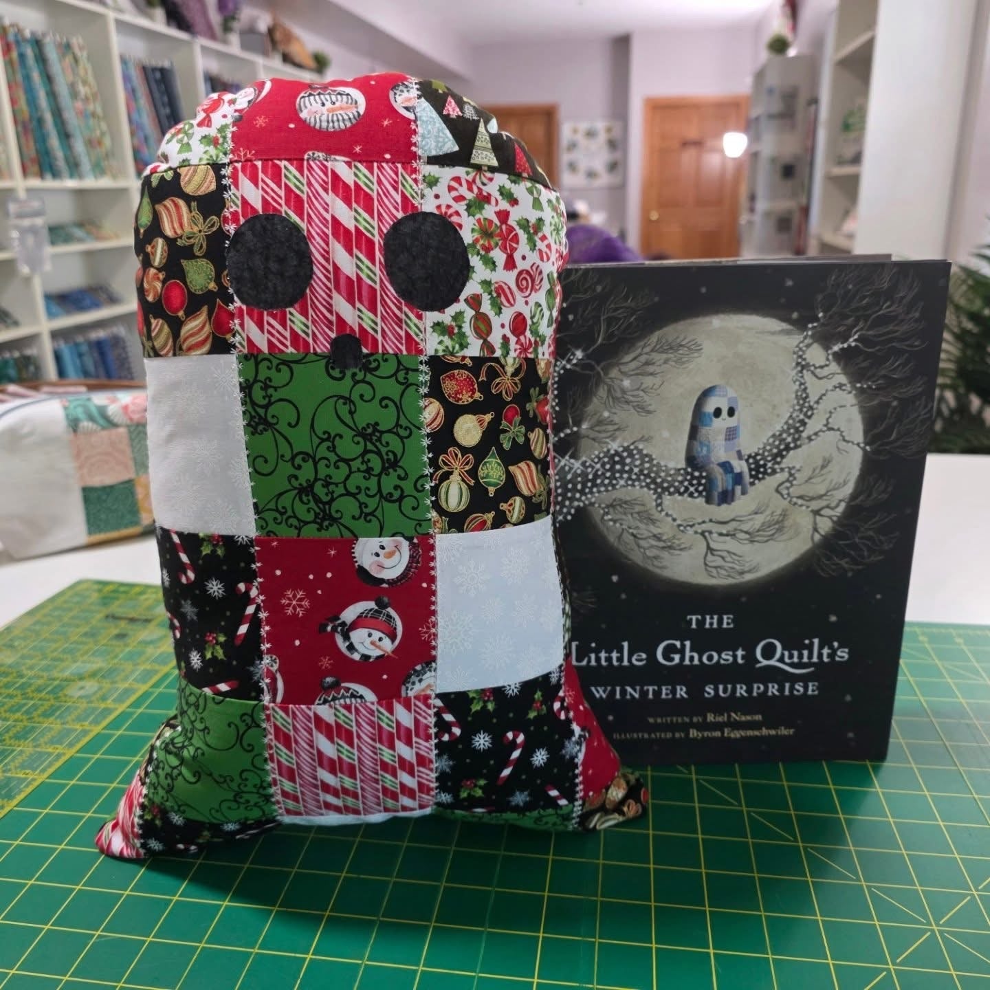 Quilted ghost-shaped pillow, red and green patchwork with black circles and blue accents