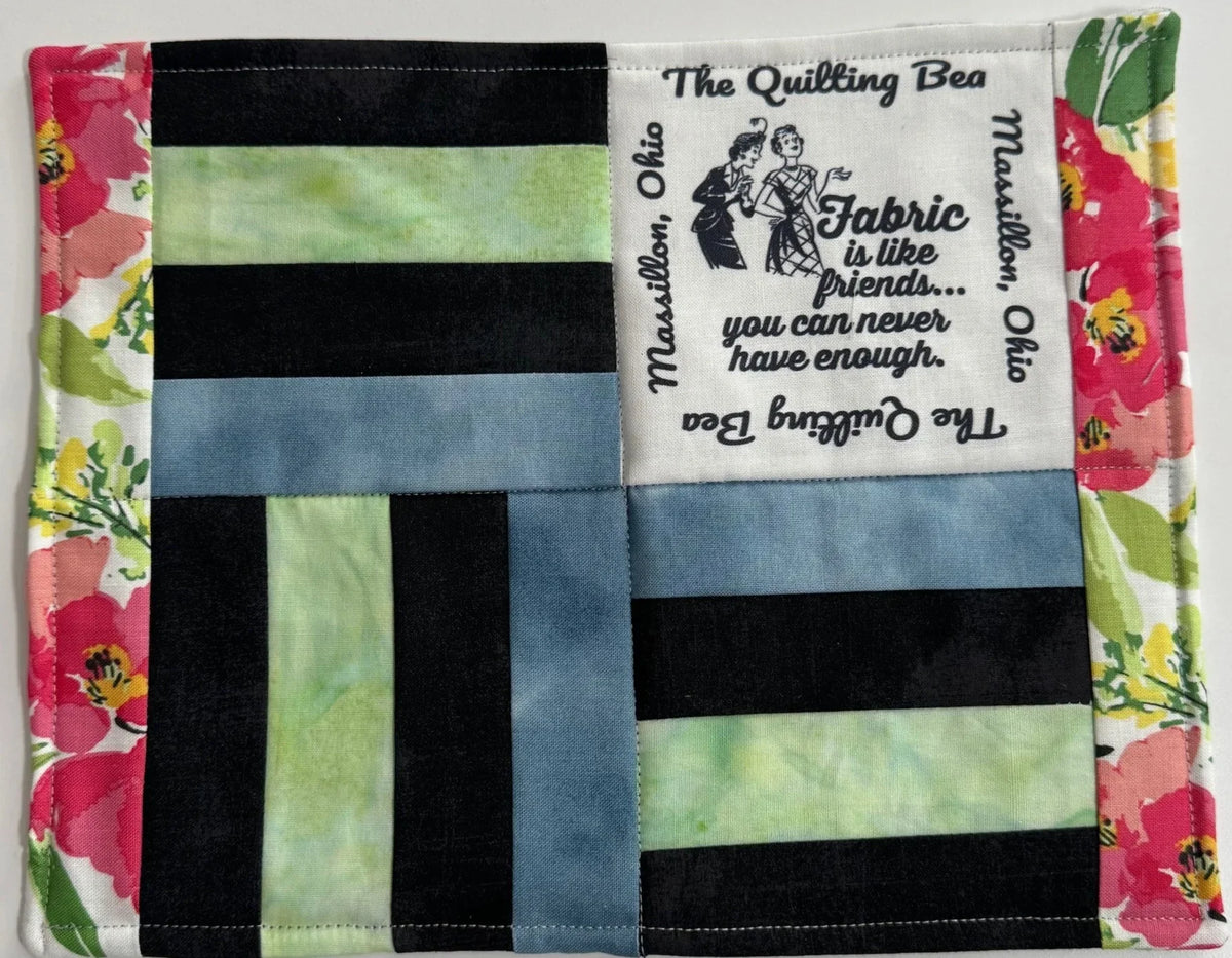 Finished mug rug with black, green, and blue striped patchwork and logo fabric label