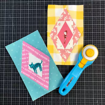 Foundation paper piecing pad with diamond quilt blocks, sample fabric pieces, and a rotary cutter.