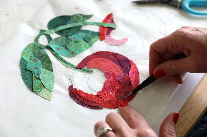 Cherry-themed fabric appliqué pieces on white cloth, hand trimming with scissors