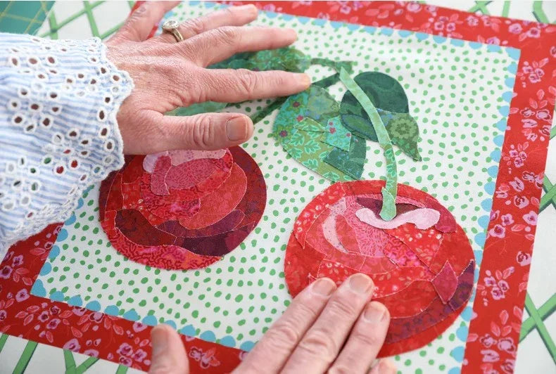 Cherry appliqué fabric square held by hands, showing red cherries and green leaves