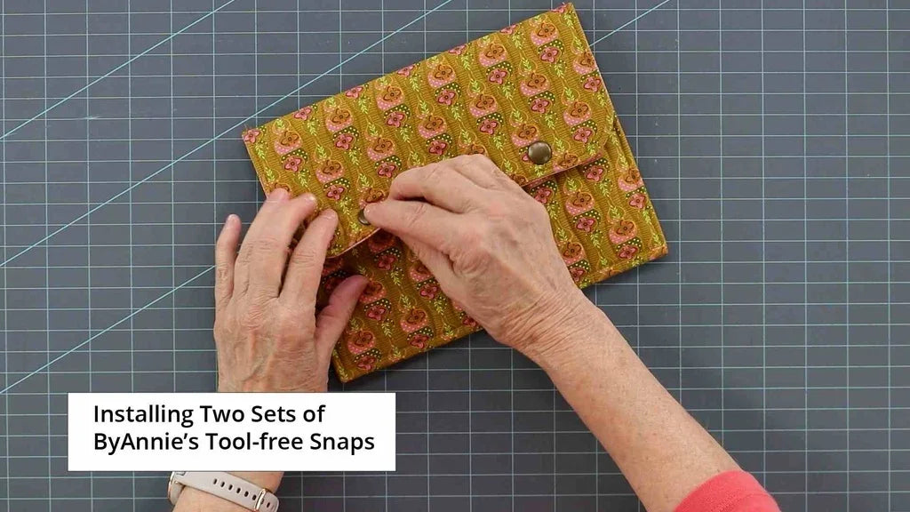 Tool-free snaps set attaching snap to green-and-pink patterned pouch using hands