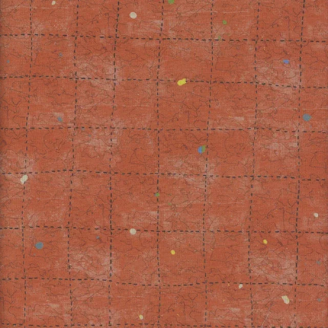 Rust red cotton fabric with faint grid lines and scattered multicolor speckles