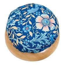 Round fabric pincushion with blue floral pattern and light wood base