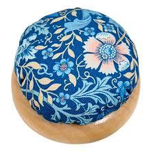 Round fabric pincushion with blue floral pattern and light wood base