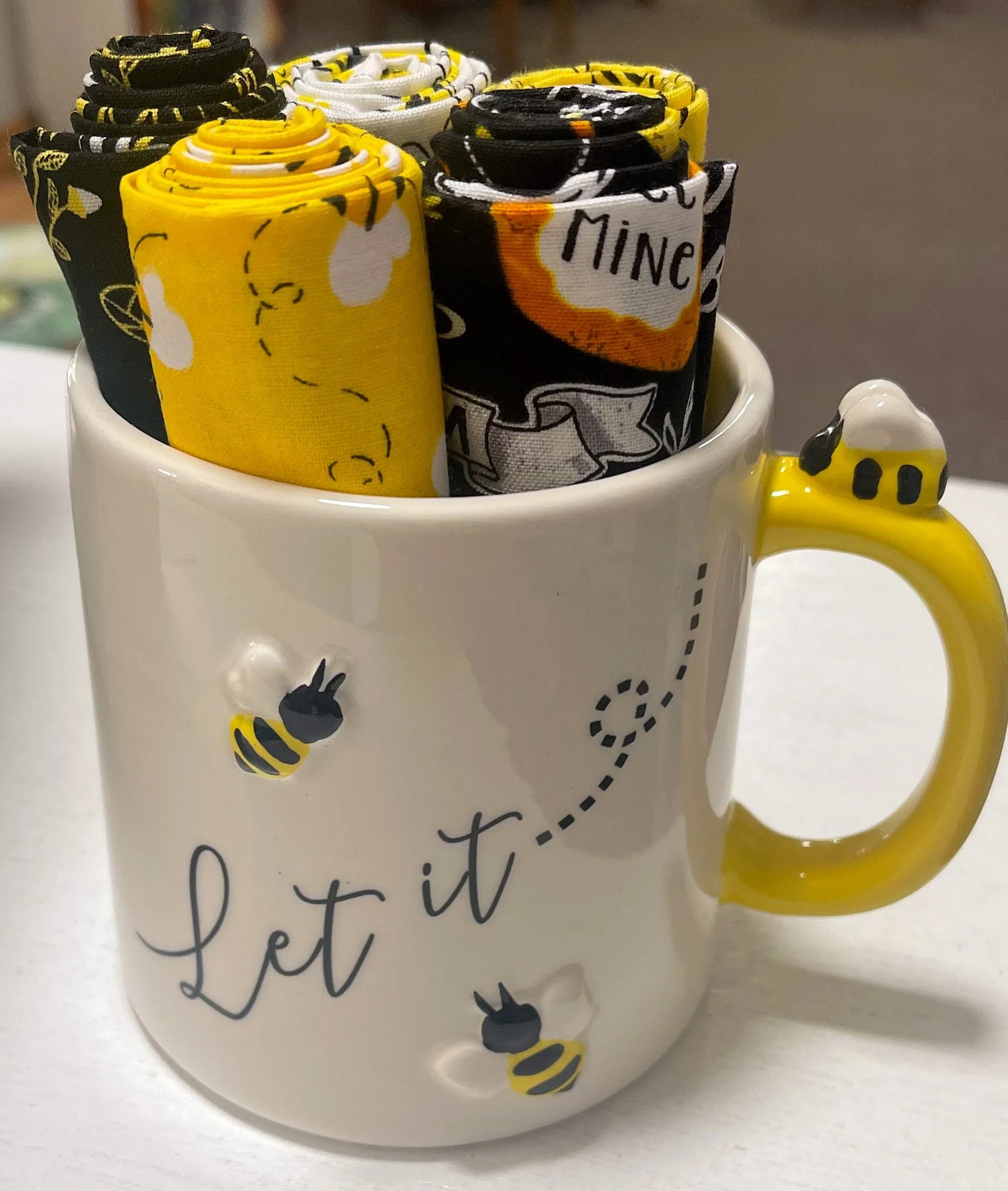 Bee ceramic mug with yellow handle and Let it lettering, holding fabric rolls