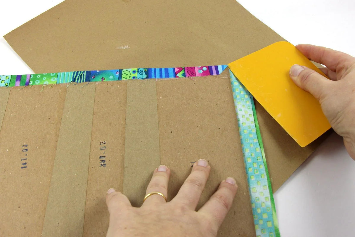 Yellow spatula smoothing patterned trim along cardboard
