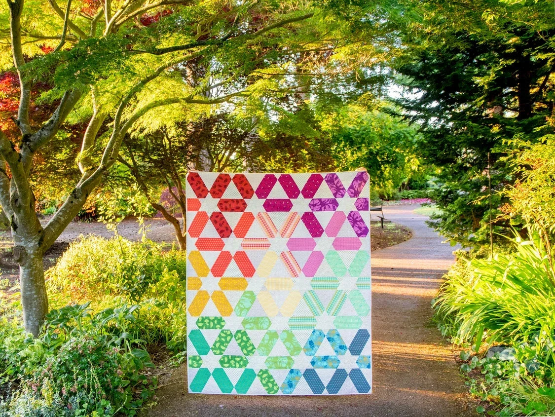Multicolor quilt top with geometric star shapes on a white background and rainbow colors.