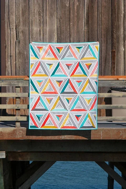 Finished quilt with repeating striped triangle blocks in teal, coral, yellow, and white