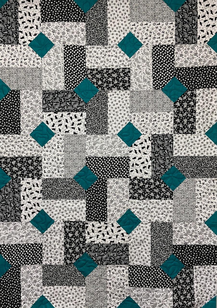Patchwork quilt pattern featuring black, white, and teal geometric blocks with diamond accents