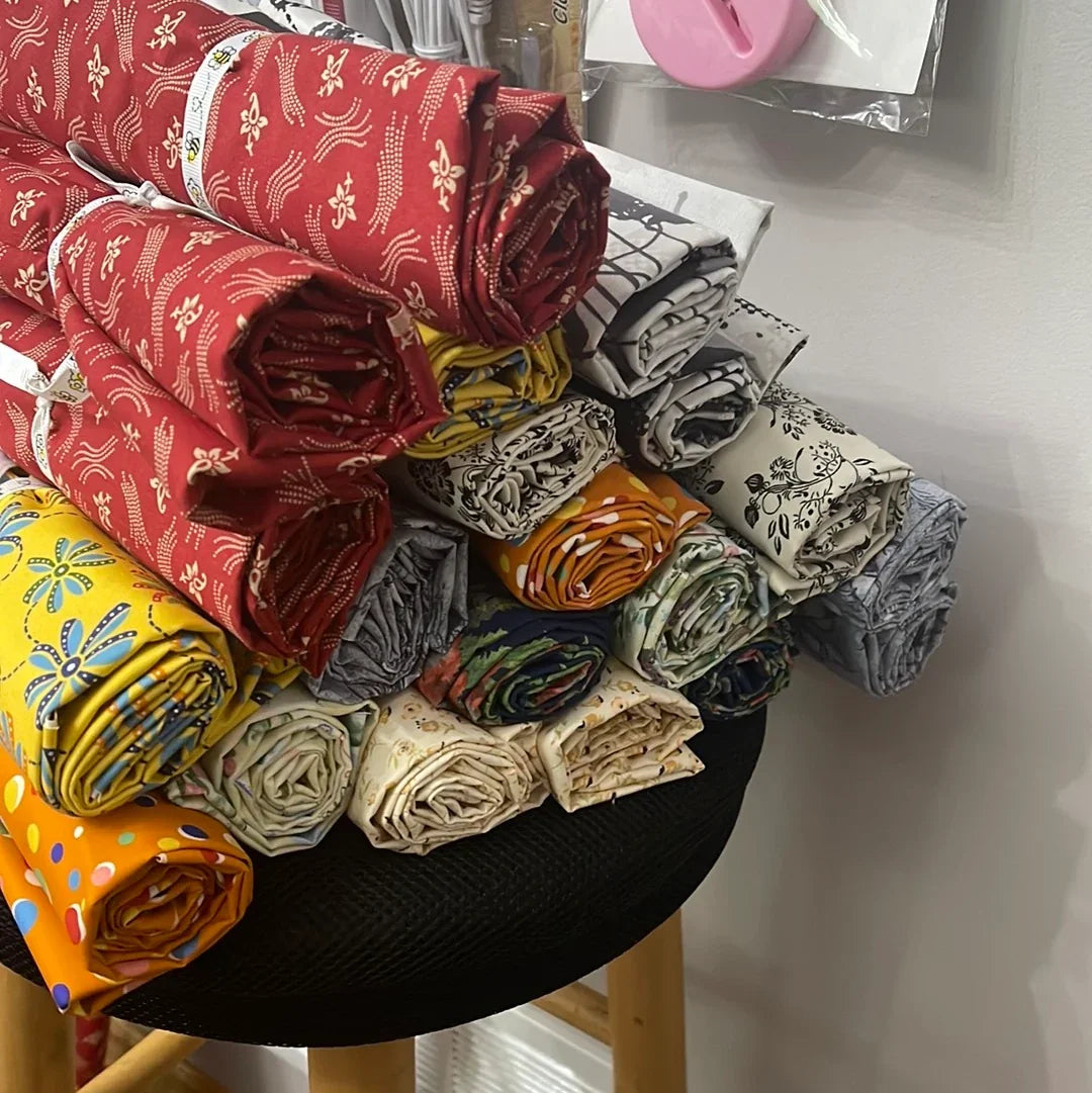 Assorted patterned fabric yard cuts, rolled bundles with red, yellow, and gray designs