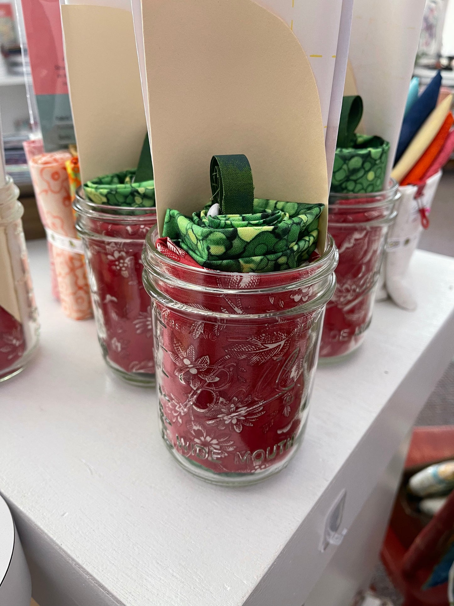Strawberry mug rug kit fabric pieces in green strips inside decorated glass jars