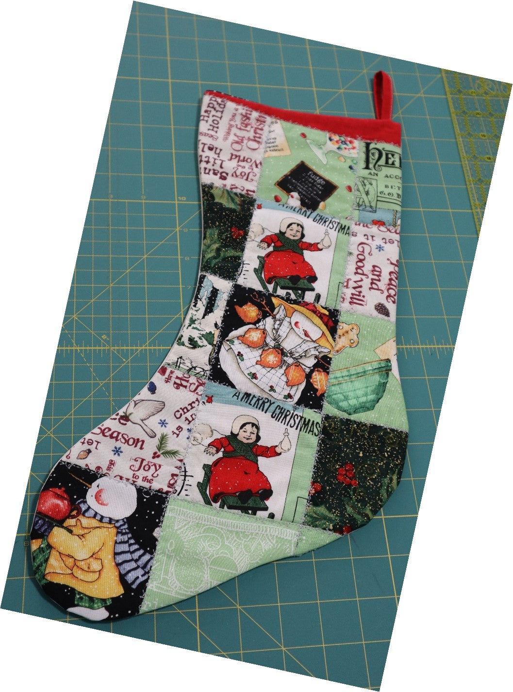Handmade patchwork Christmas stocking with holiday-themed fabric squares on a green cutting mat.