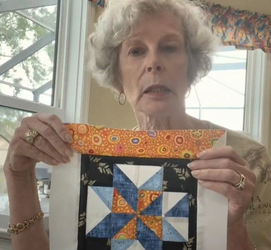 Elderly woman holding a blue and orange star quilt block and matching fabric strip.