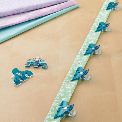 Triple wide Wonder Clips securing quilt strips, teal clips on fabric