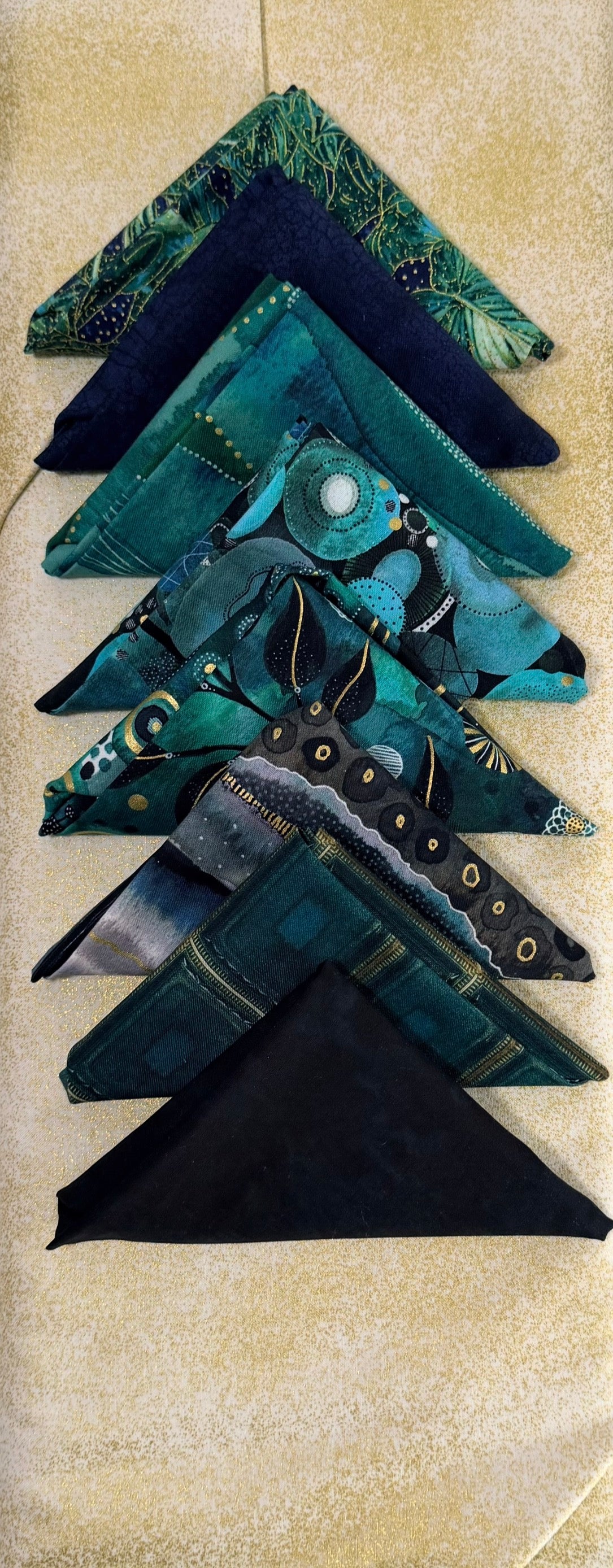Folded dark teal and green fabric charm pieces with stitched patchwork accents
