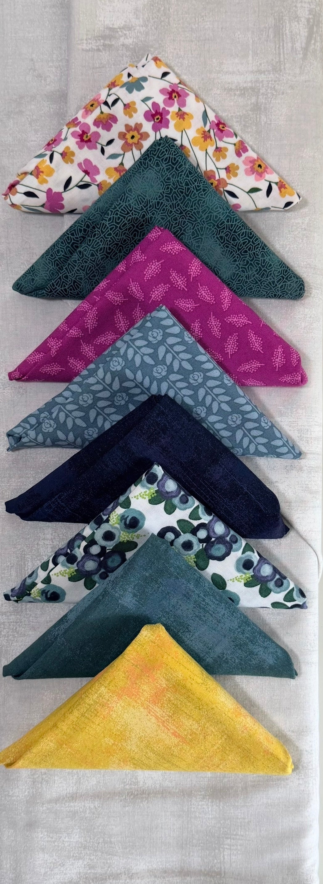Set of five folded patterned fabric pieces with floral, teal, magenta, and dark designs