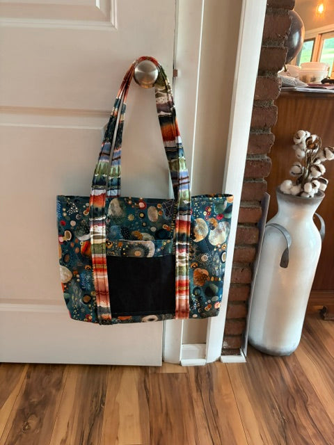 Handmade quilted tote bag with celestial print and colorful stripes hanging on a door knob.